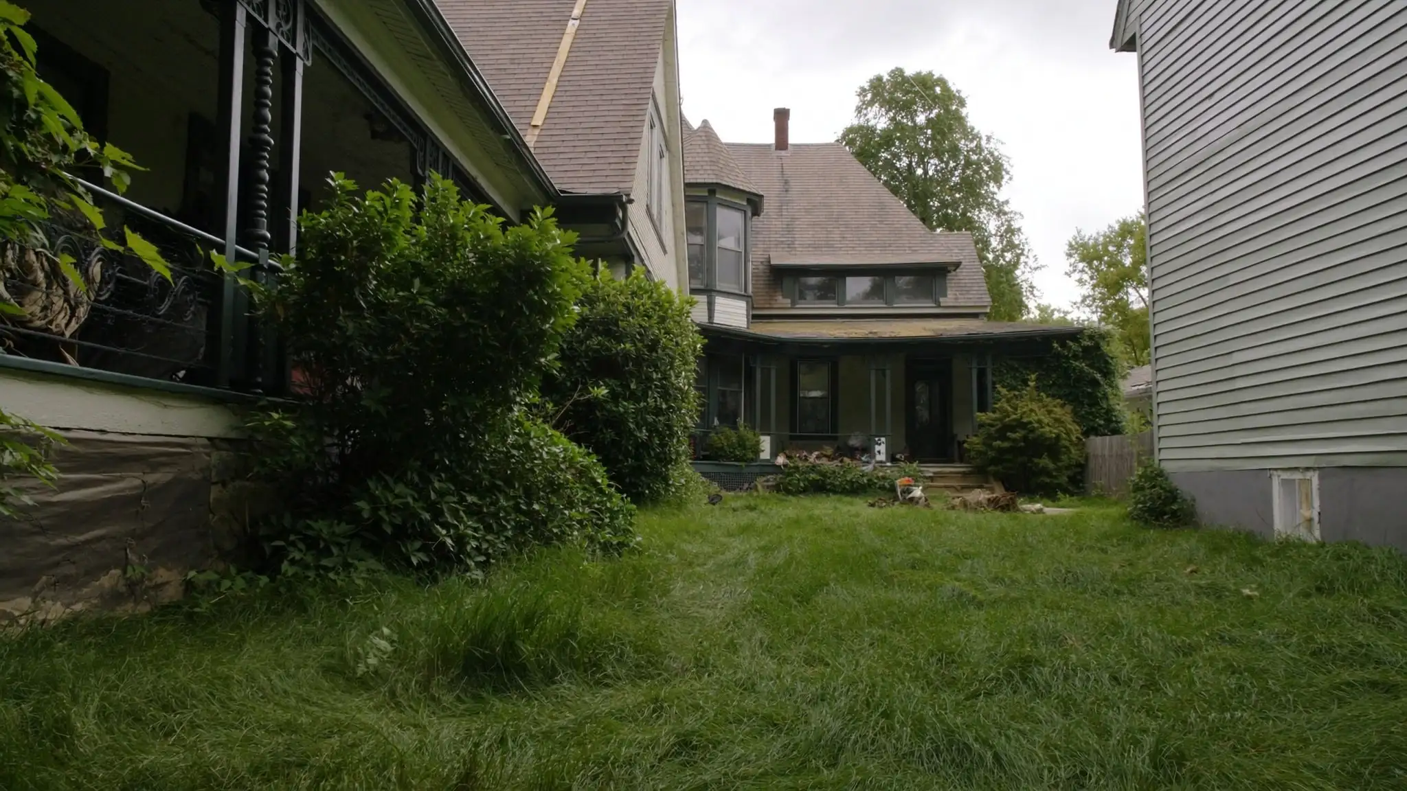 Overgrown front yard in front of an older vacant house