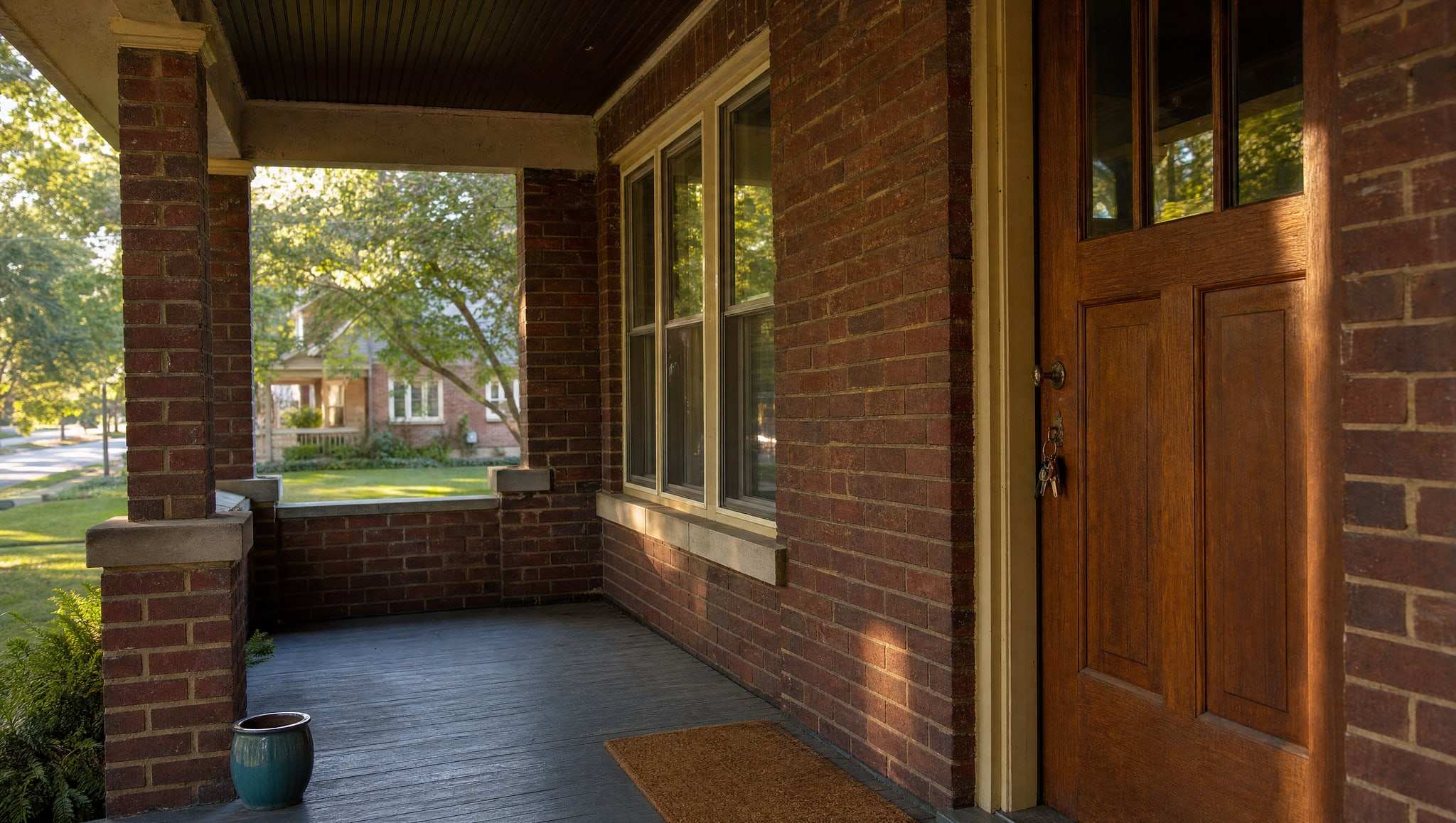 Front porch and door of a brick bungalow with keys in the lock