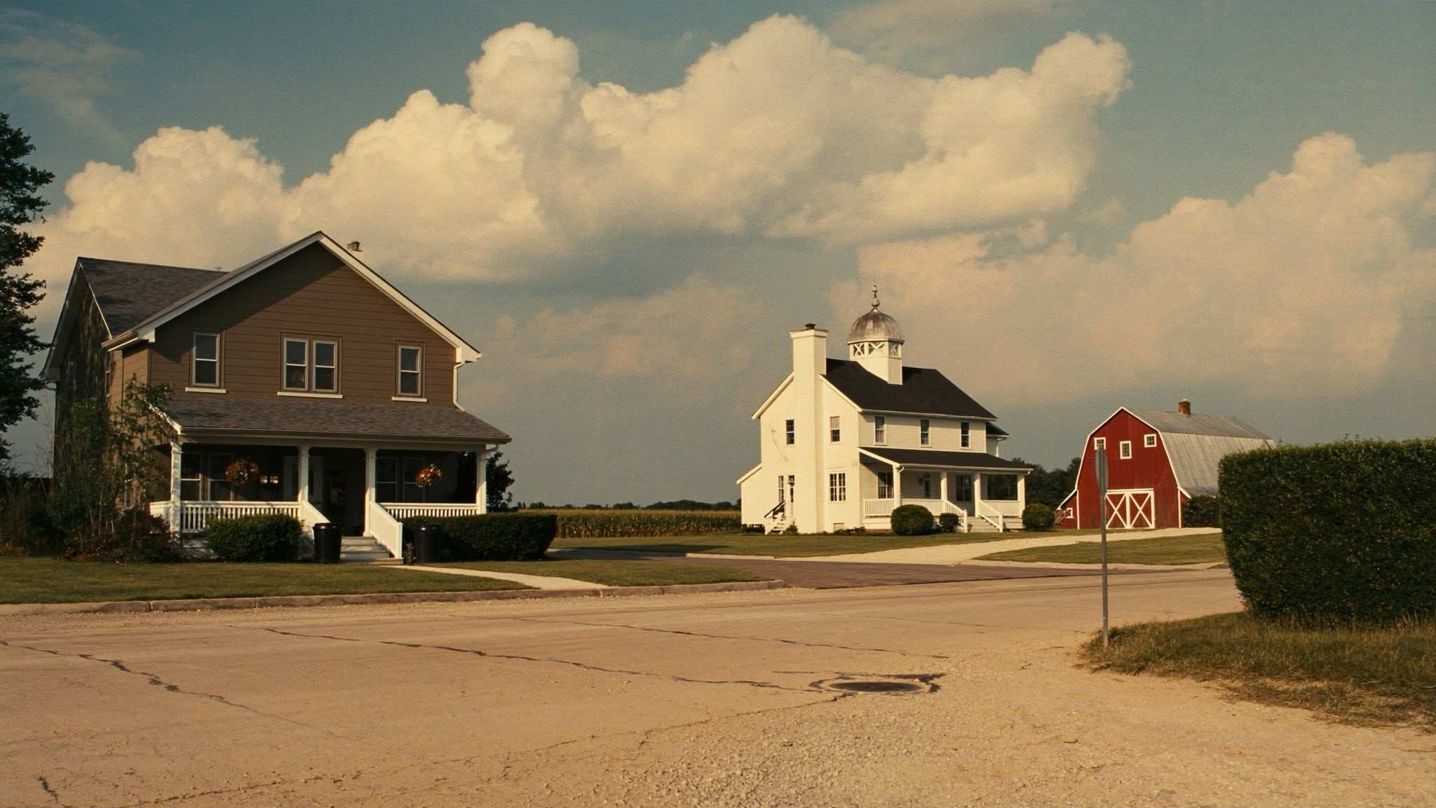 Two-story homes and a farmhouse with a red barn at the edge of farm fields