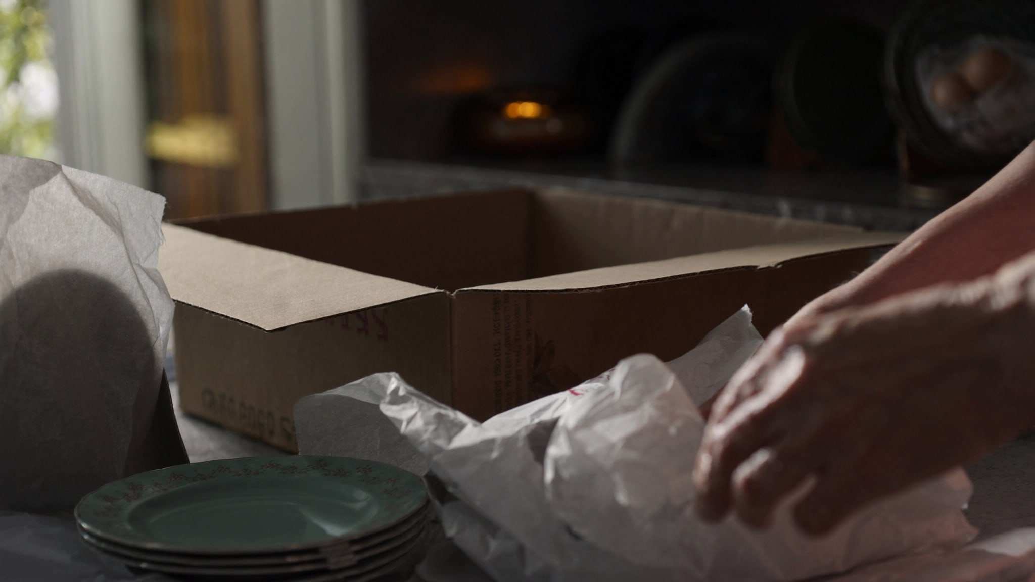 Hands wrapping dishes in packing paper next to a moving box